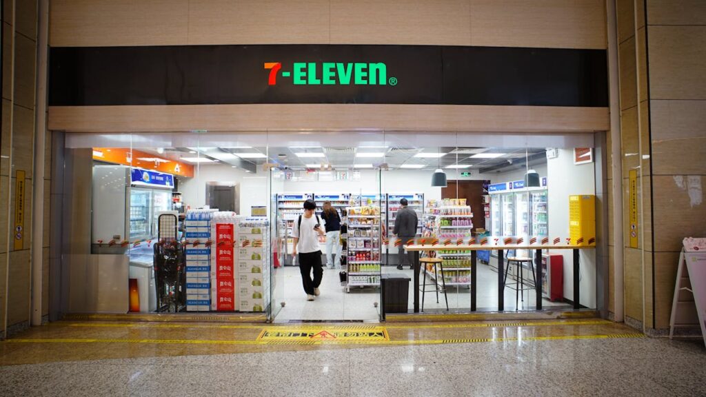 Indoor view of a 7-Eleven store entrance with people shopping and products displayed.