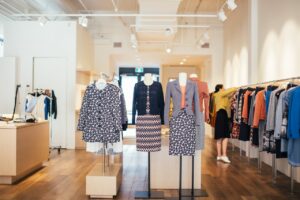 Side view of unrecognizable female seller standing and adjusting stylish colorful clothes hanging on rail in boutique in daytime